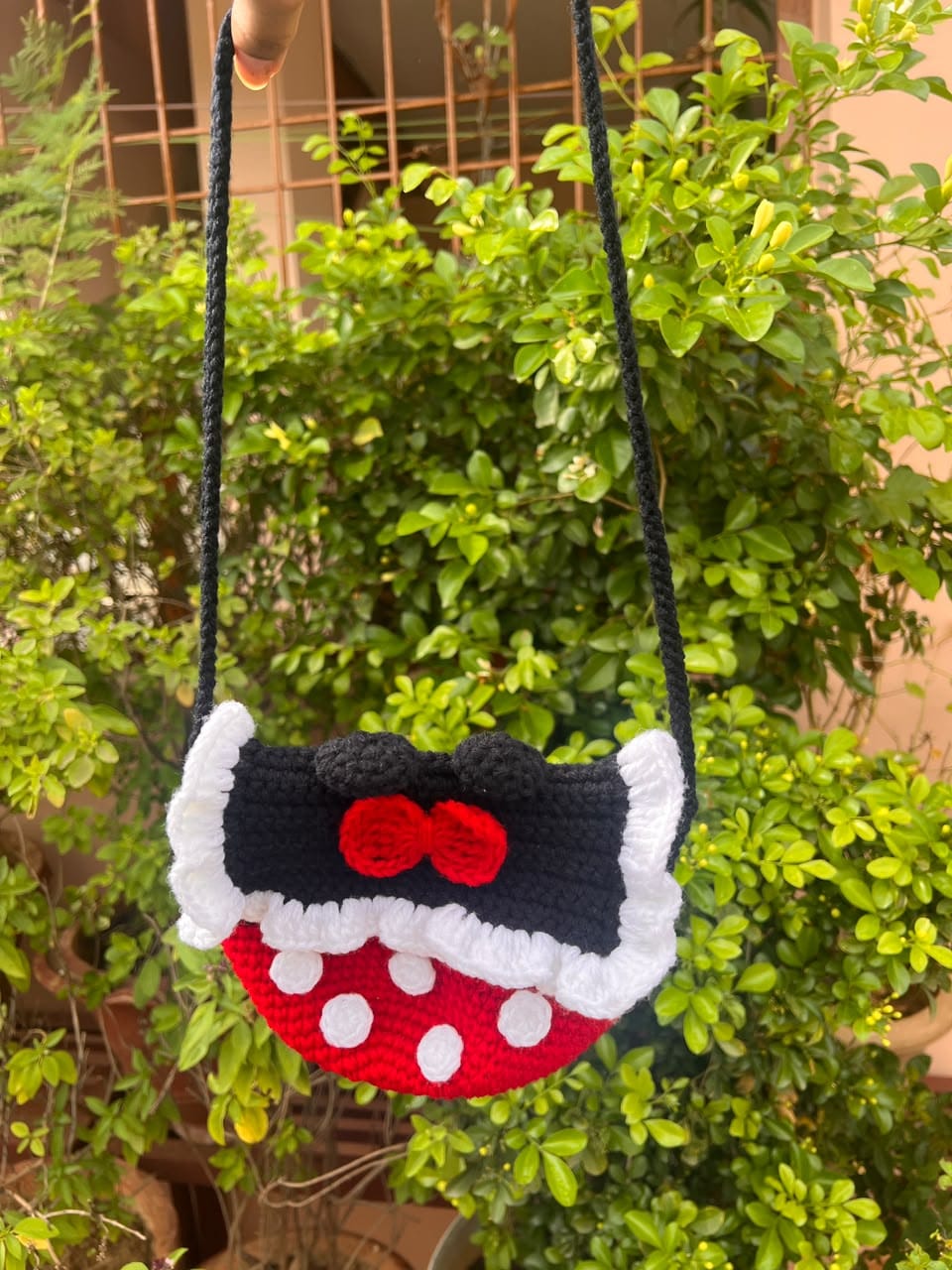 A red and black crochet shoulder bag with white polka dots, white ruffles and a red bow