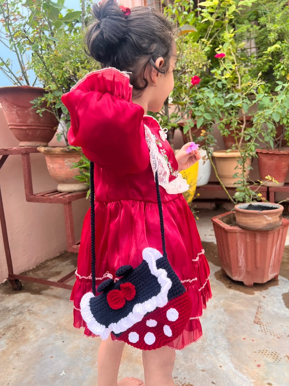 A child wearing the Polka Dot Bow Bag, showing the black shoulder strap and red polka-dot base