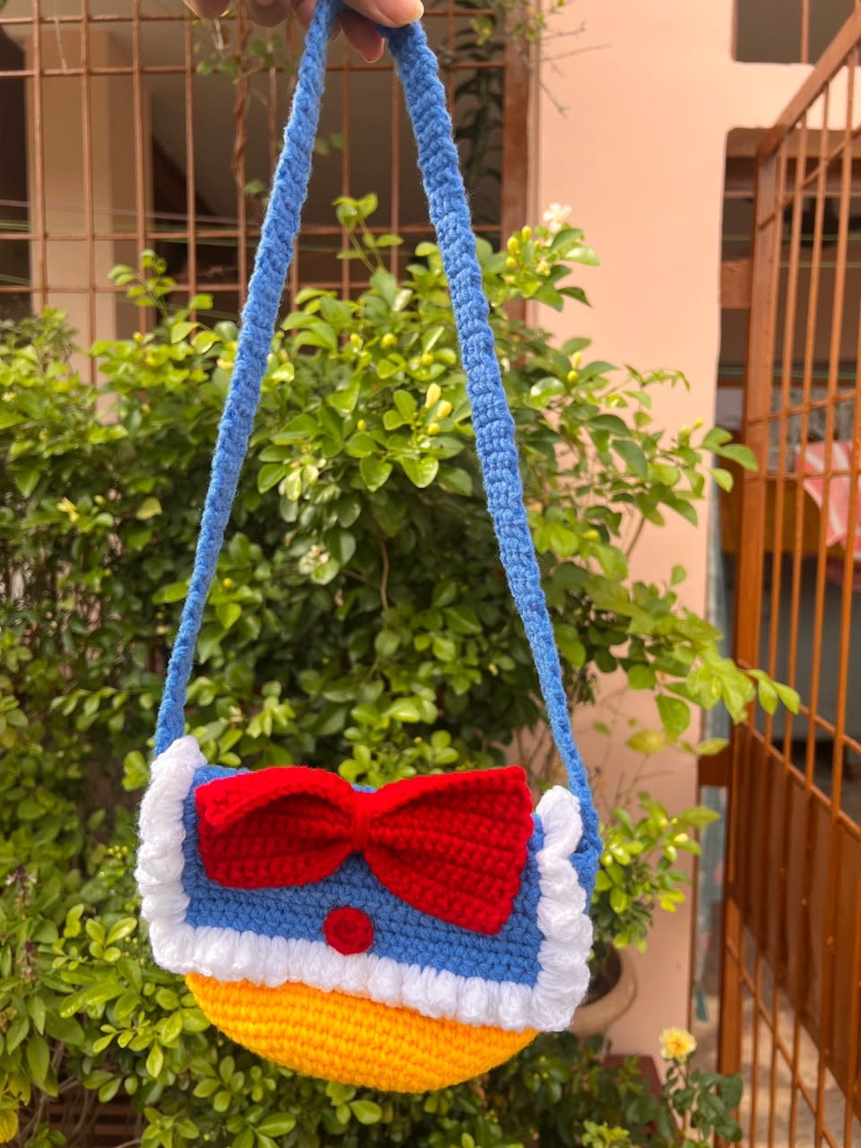 A blue and yellow crochet shoulder bag with a large red bow and white ruffled trim