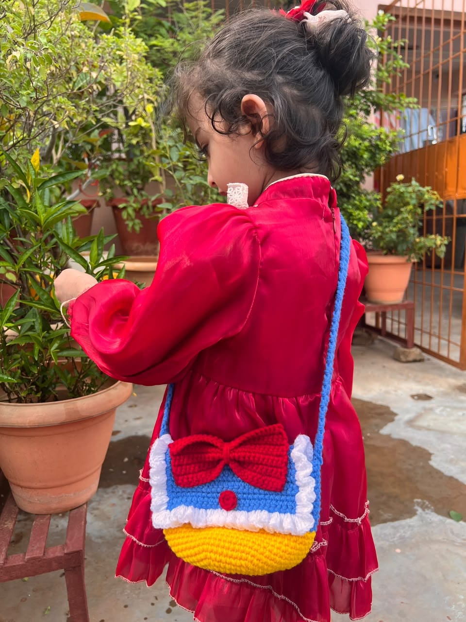 A child wearing the Sailor Bow Bag, showing its blue strap, red bow and yellow base