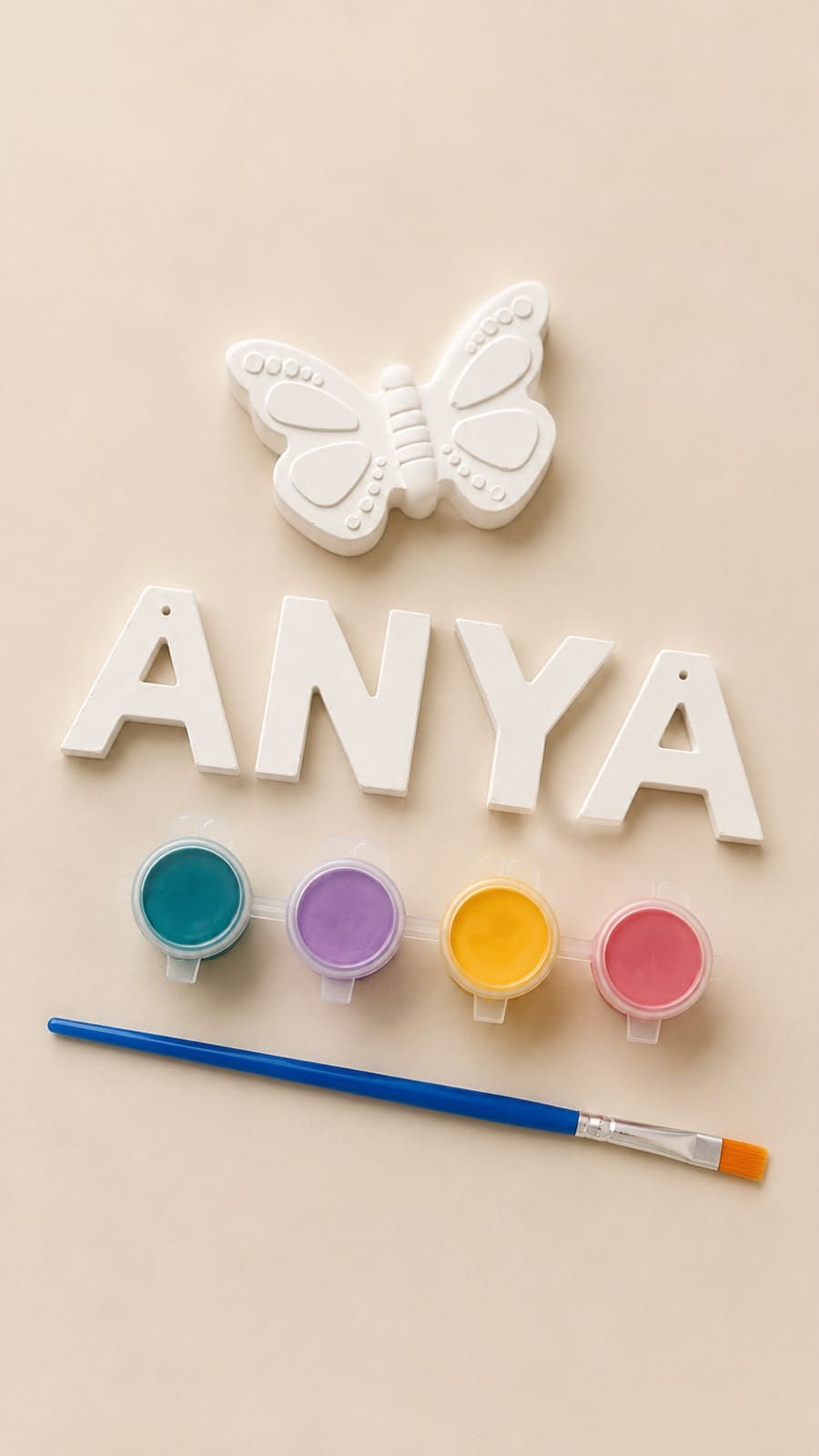 Unpainted plaster letters spelling "ANYA" with a plaster butterfly, four paint pots and a brush