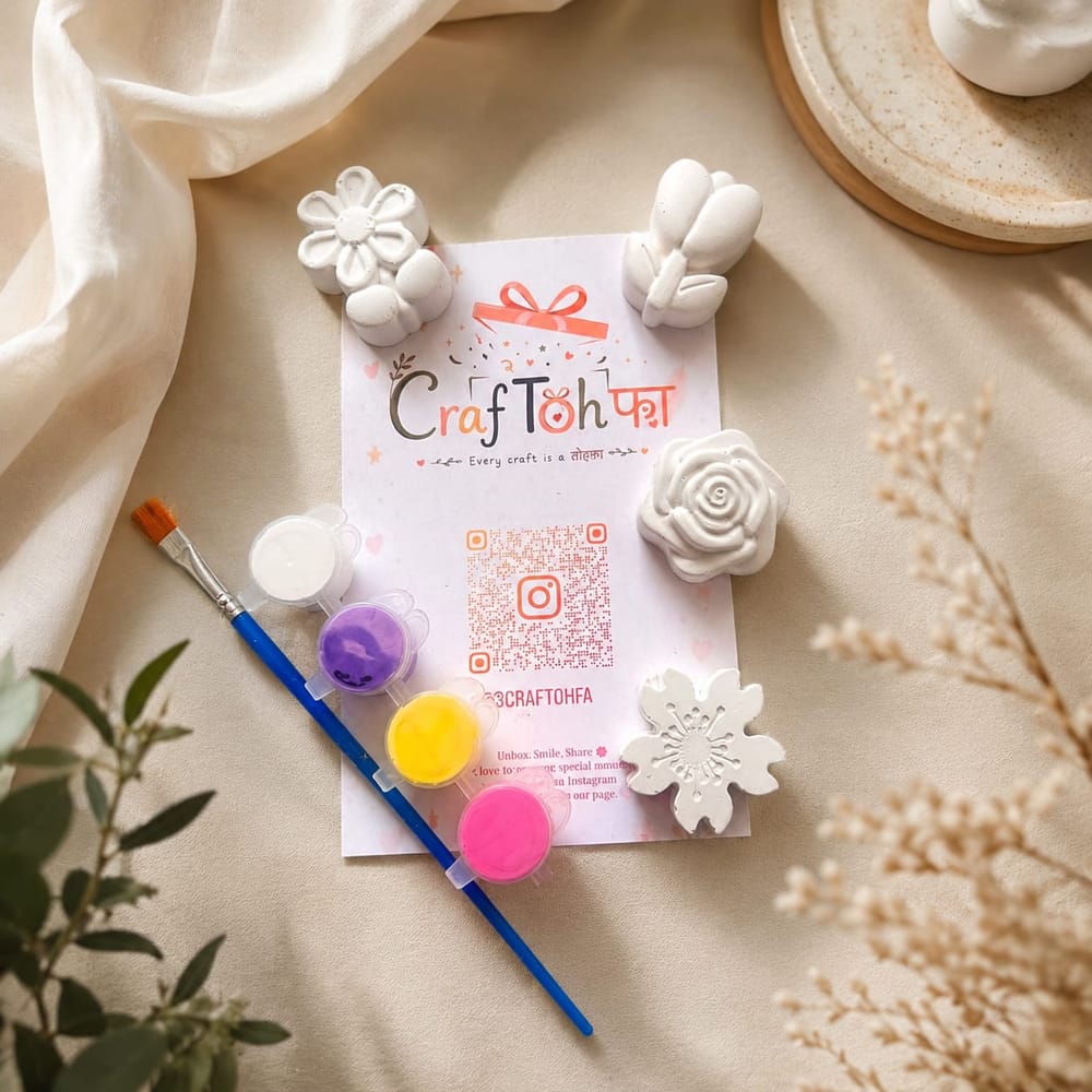Four unpainted plaster flowers (a daisy, a rose, a tulip bunch and a cherry blossom) with white, purple, yellow and pink paint pots and a brush on a printed Craftohfa card