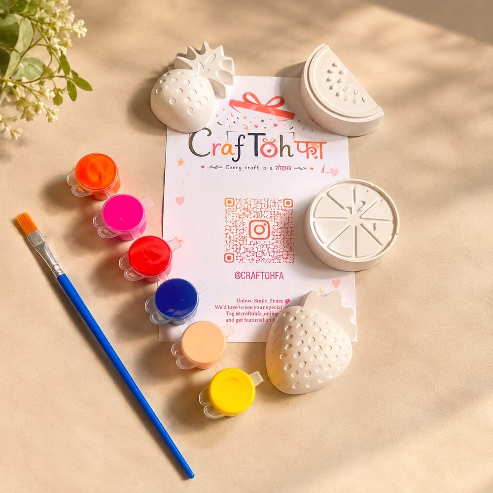 Four unpainted plaster fruits (a strawberry, a pineapple, a watermelon slice and an orange slice) with six paint pots and a brush around a printed Craftohfa card