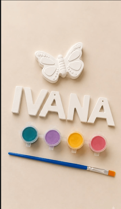 Unpainted plaster letters spelling "IVANA" below a plaster butterfly, with teal, lilac, yellow and pink paint pots and a brush