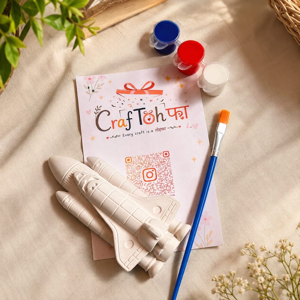 An unpainted plaster space shuttle with two booster rockets, beside blue, red and white paint pots and a brush on a printed Craftohfa card