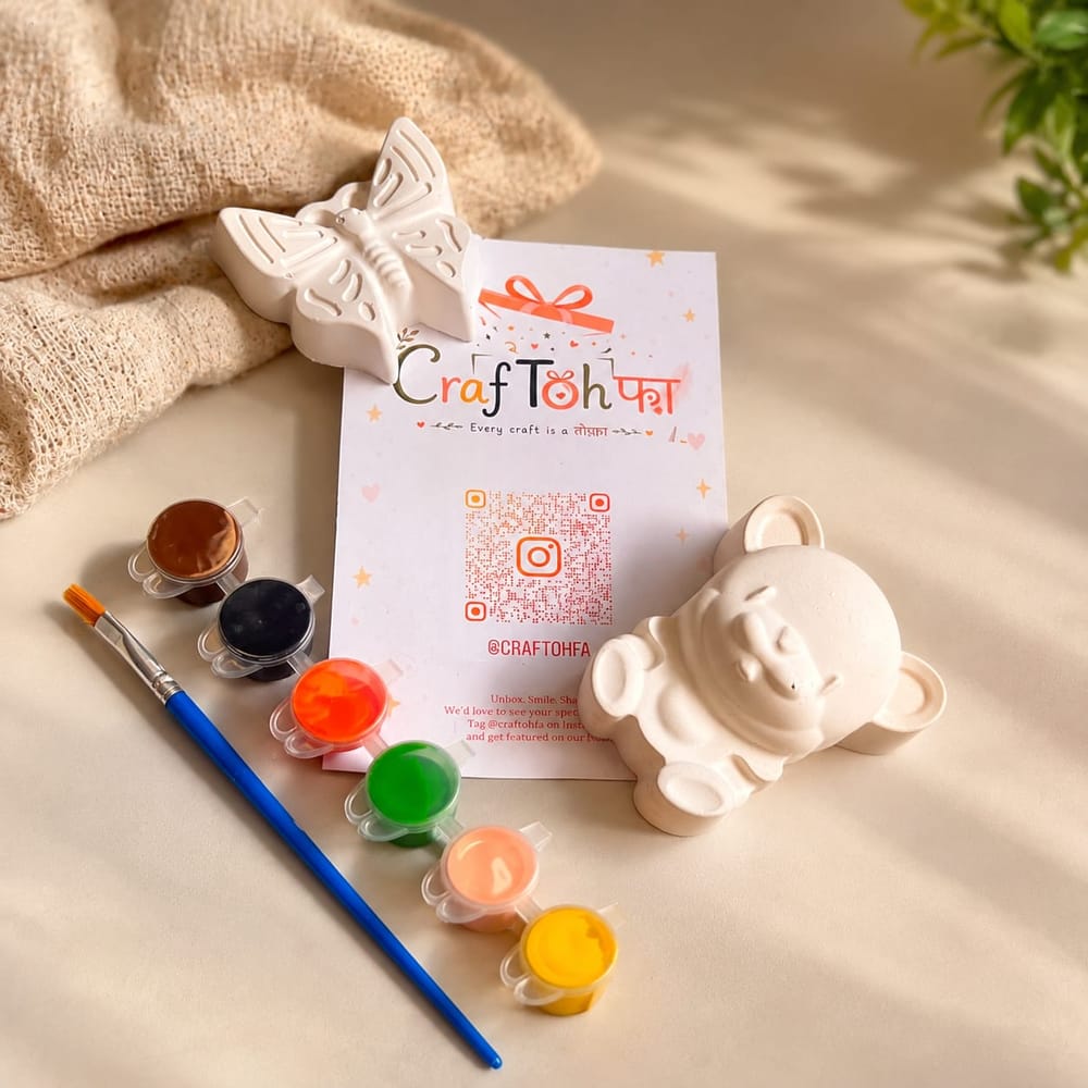 An unpainted plaster butterfly and teddy bear with six paint pots and a brush around a printed Craftohfa card